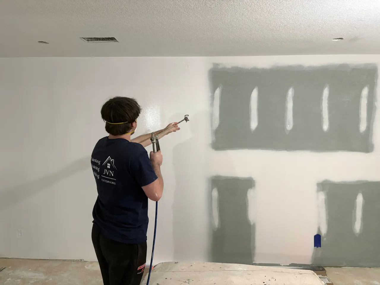JVN Exteriors painter spraying interior wall paint over drywall repairs with floors covered